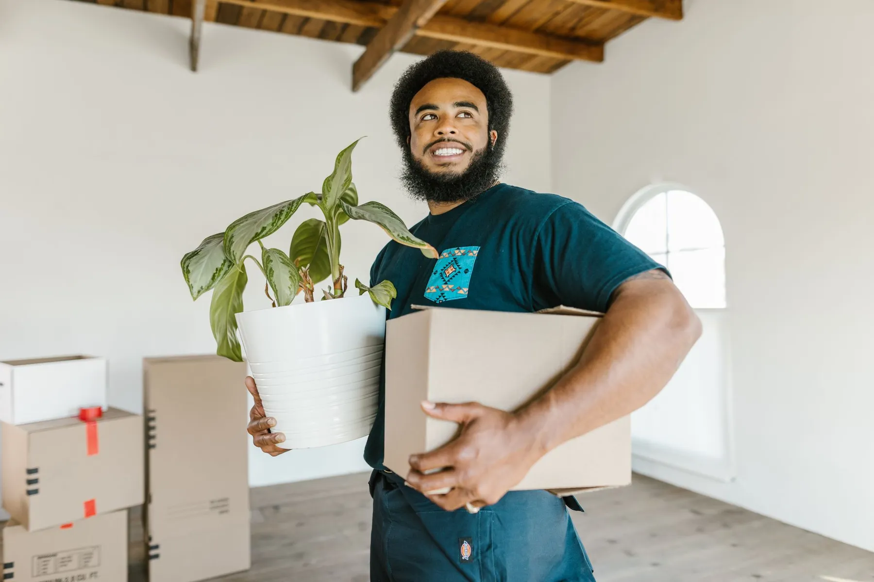 Mover smiling while carrying a moving box and a potted plant