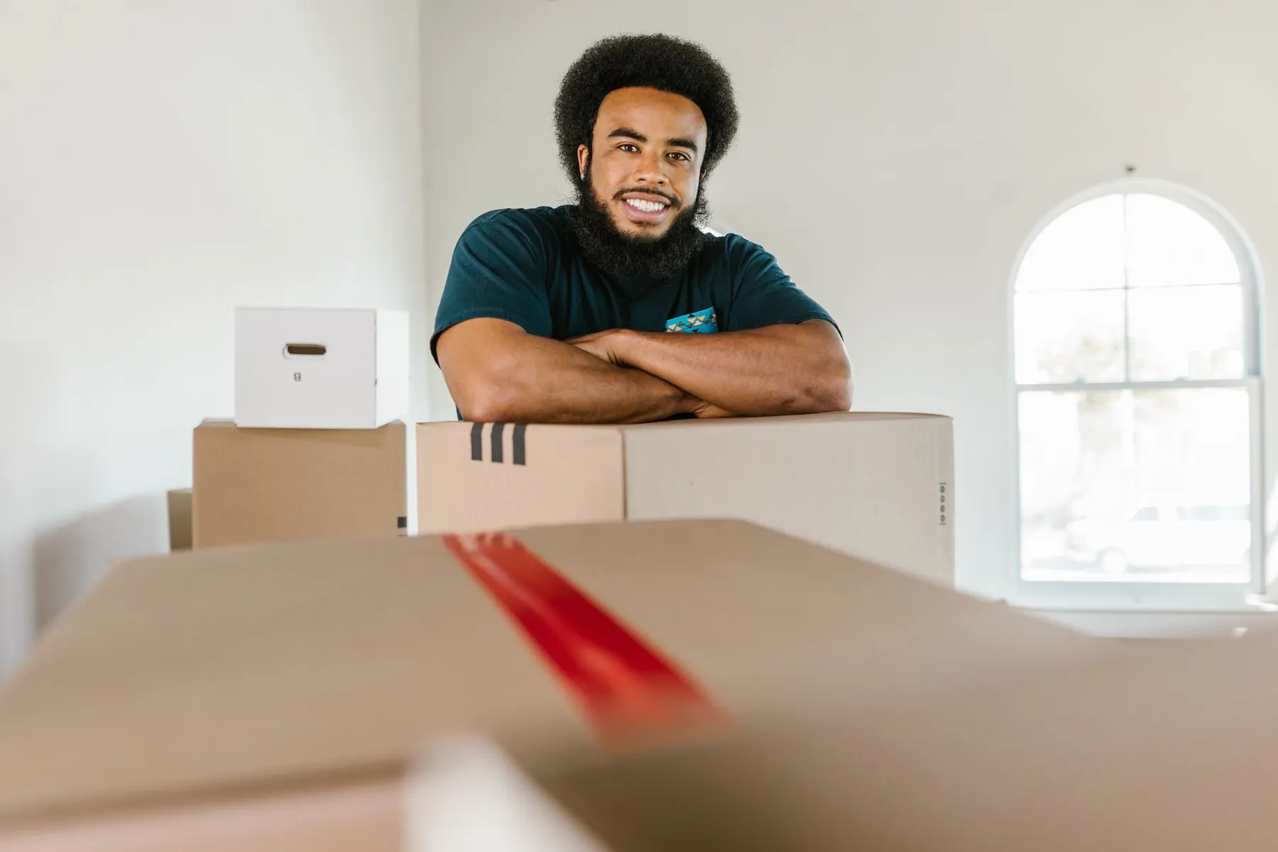 Smiling mover in a teal uniform leaning on a stack of moving boxes
